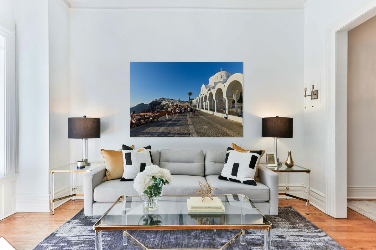 Crowds walk past white church cliffside town in Santorini.
