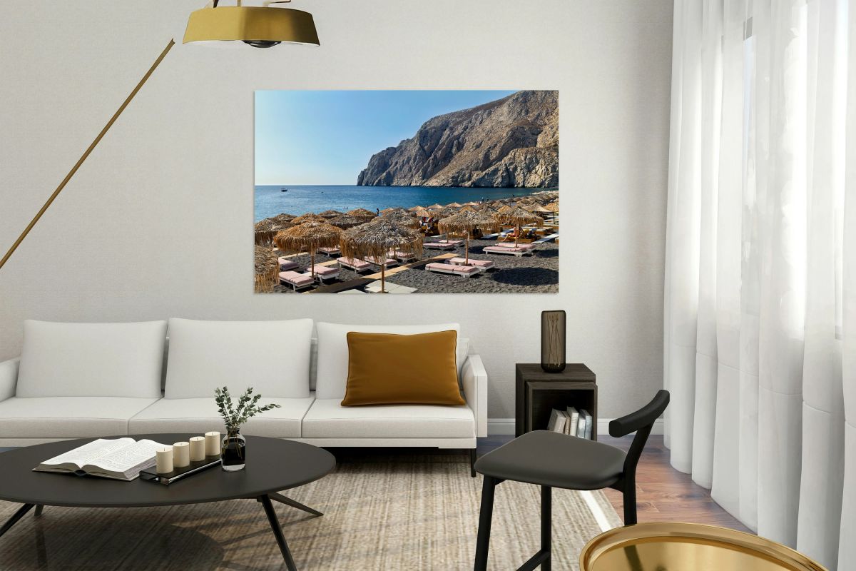 Scenic black sand beach with straw umbrellas and rocky cliffs.