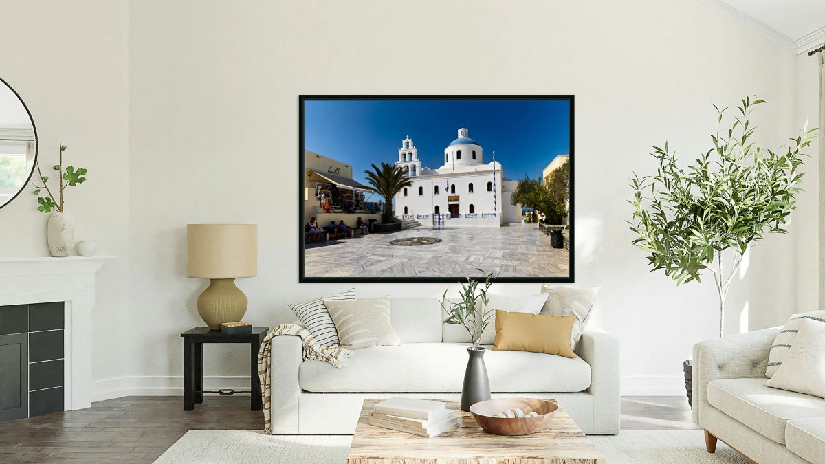 White Greek church with blue dome in sunny town square.