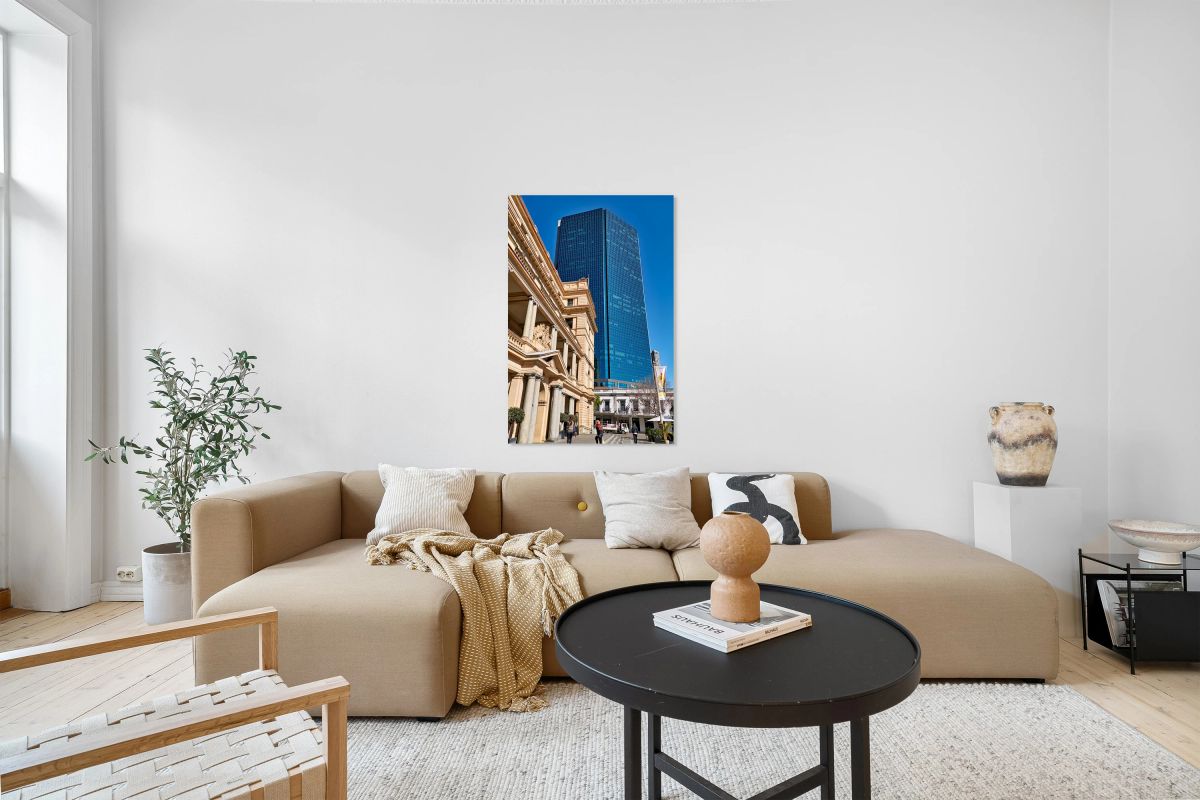 Modern skyscraper dwarfs historic building under clear blue sky.