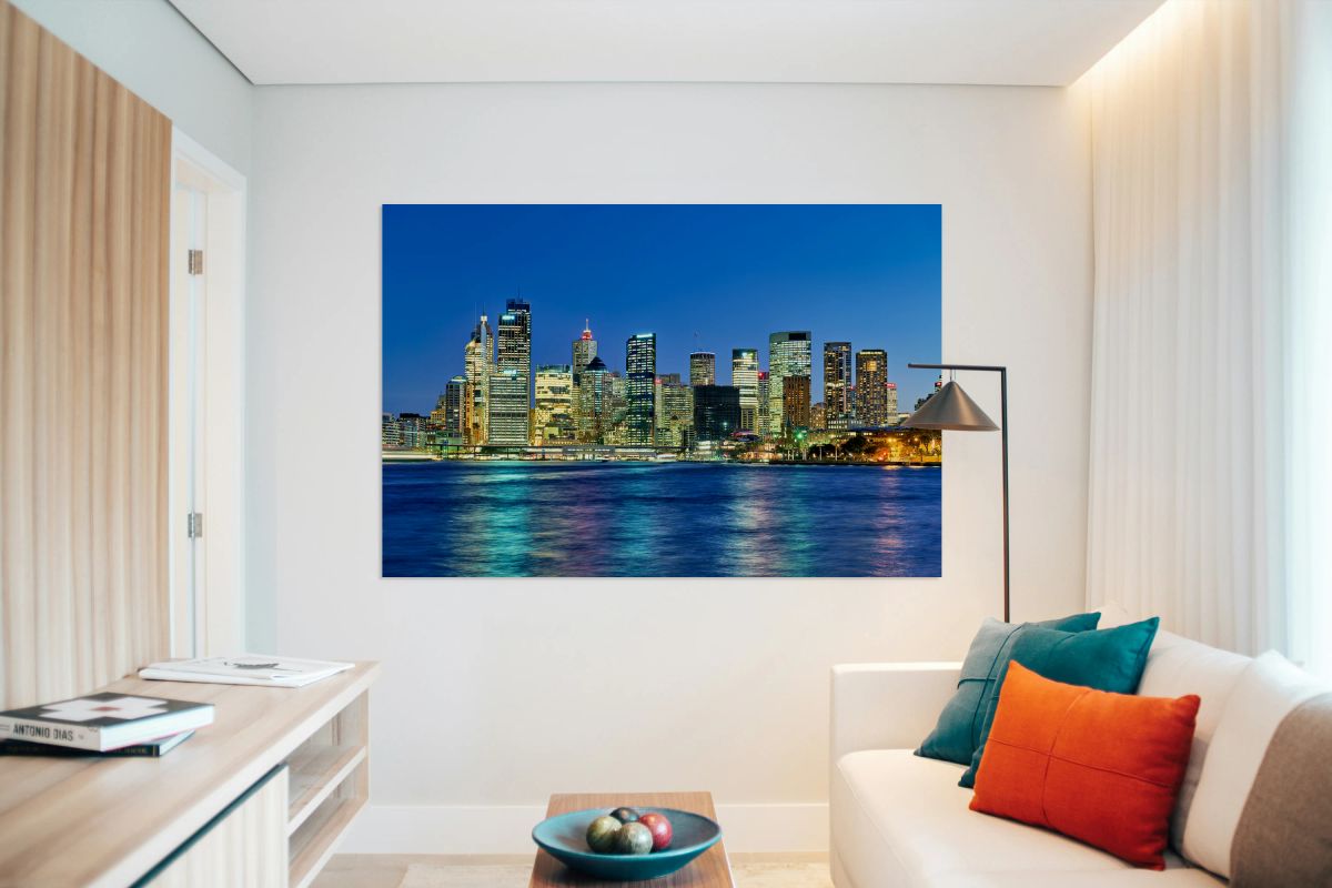 Sydney skyline at dusk with illuminated buildings and water.