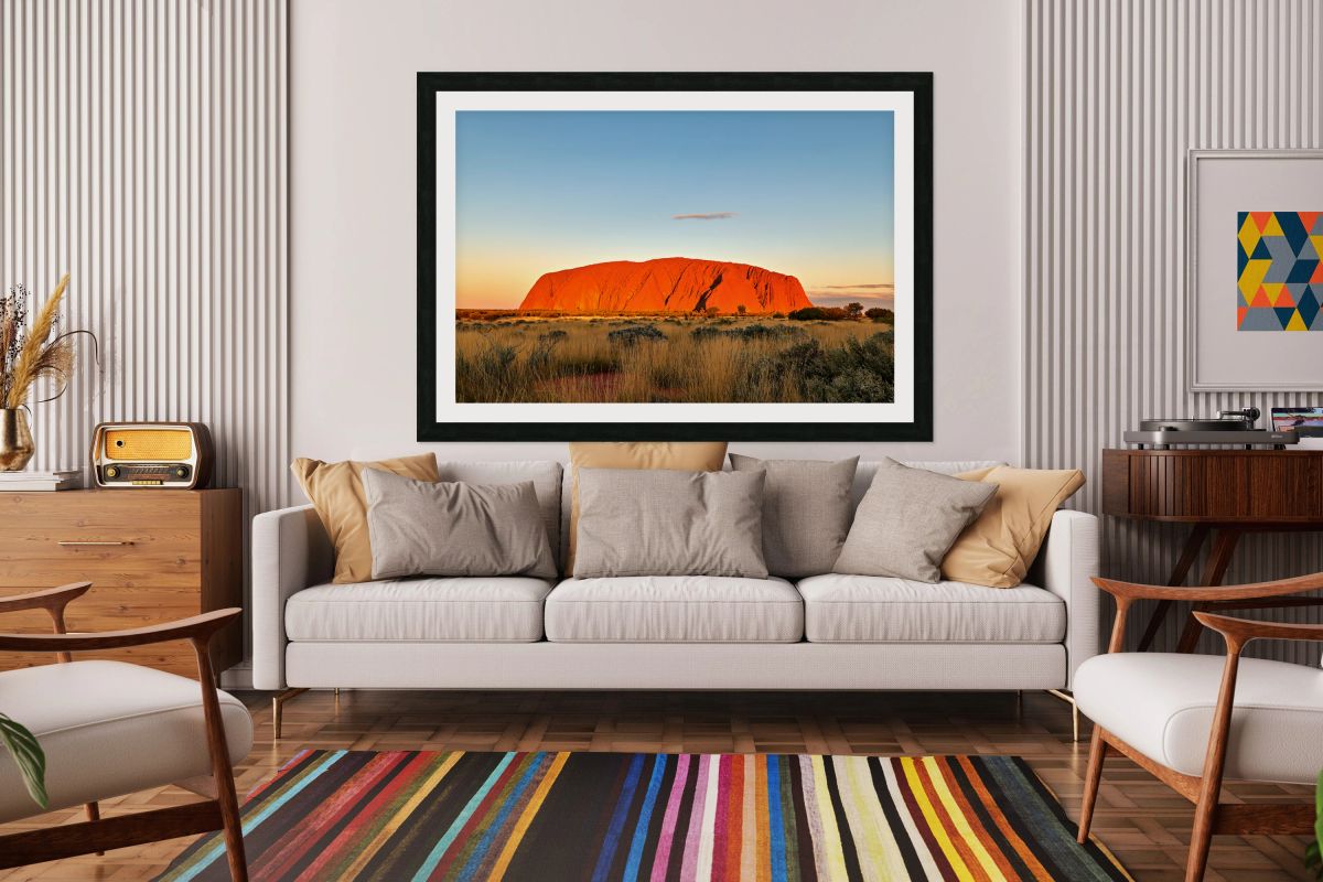 Uluru glows orange at sunset with a vast grassy plain.