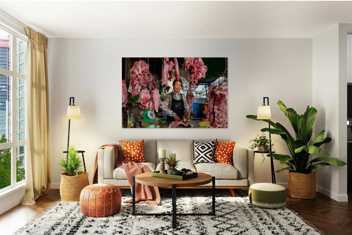 Woman butcher at market stall with hanging raw meat.