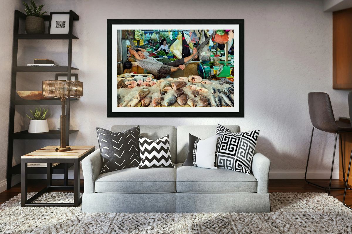 Market vendor relaxes in hammock above fresh fish.