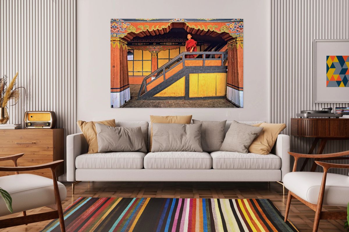 Young monk in red robes on colorful temple staircase.