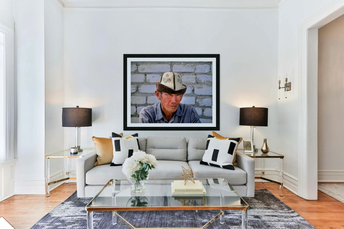 Man in traditional hat sits against a brick wall in Bukhara